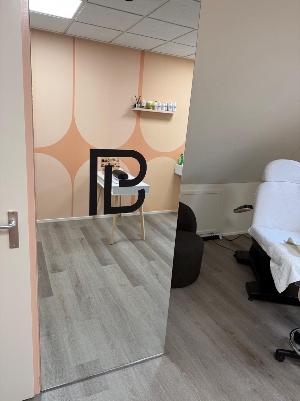Interieur van Pedicurestudio Blanche met het bedrijfslogo, perzikkleurig wandpatroon en de behandelstoel